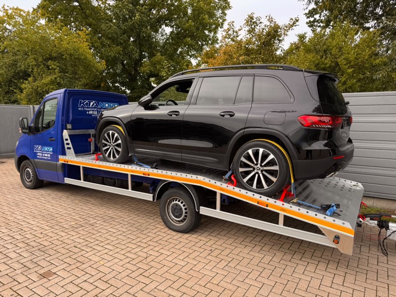 Schwarzer SUV auf der Plattform des Transporters, an den Rädern mit Gurten gesichert
