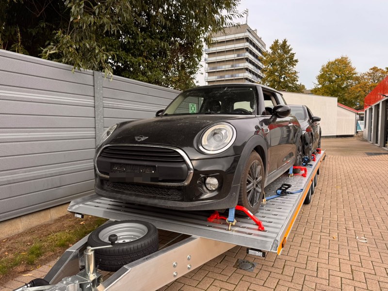 Schwarzer Kleinwagen auf dem Anhänger, dahinter ein weiteres verladenes Fahrzeug